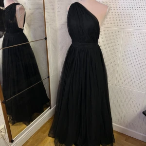 Svart långklänning med oneshoulder - Elegant svart långklänning med oneshoulder-design. Klänningen har ett flödande tyg som ger en vacker siluett och är perfekt för speciella tillfällen. I fint skick. Storlek XS. 