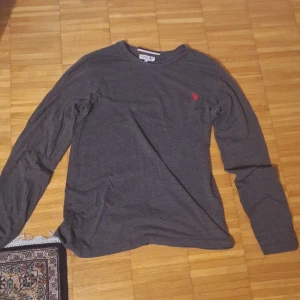 Grå långärmad tröja från Ralph Lauren - Säljer en stilren grå långärmad tröja från Ralph Lauren med en liten röd logga på bröstet. Tröjan är i en mjuk och bekväm bomullskvalitet. Kan ändra pris om bud.