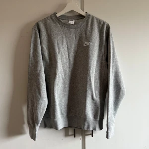Grå sweatshirt från Nike - Säljer en klassisk grå sweatshirt från Nike med rund hals och långa ärmar. Tröjan har en liten Nike-logga på bröstet och är tillverkad i mjukt material för extra komfort. Perfekt för en avslappnad stil. lite nopprig annars bra skick. 
