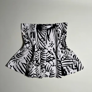 Topp - Snygg svartvit topp som man kan ha som kjol oxå från Jennifer Taylor med ett unikt grafiskt mönster. Kjolen har en volangdetalj som ger en fin form och rörelse. Perfekt för att ge din outfit en stilfull touch. 🖤🤍