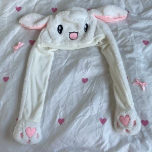 Vit kaninmössa med öron  - Söt vit mössa i form av en kanin med långa öron och rosa detaljer. Mössan har ett gulligt ansikte framtill och rosa hjärtan på tassarna. Perfekt för att hålla sig varm och se bedårande ut samtidigt!💗(KOM GÄRNA MED PRISFÖRSLAG💘) 