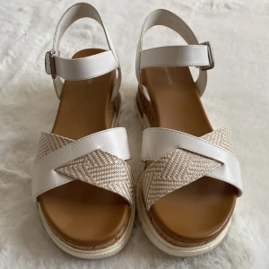 Vita sandaler från Graceland - Snygga vita sandaler från Graceland med korsade remmar i syntet och ett mönstrat tyg. Sandalerna har en bekväm korksula och justerbart spänne vid ankeln för perfekt passform.