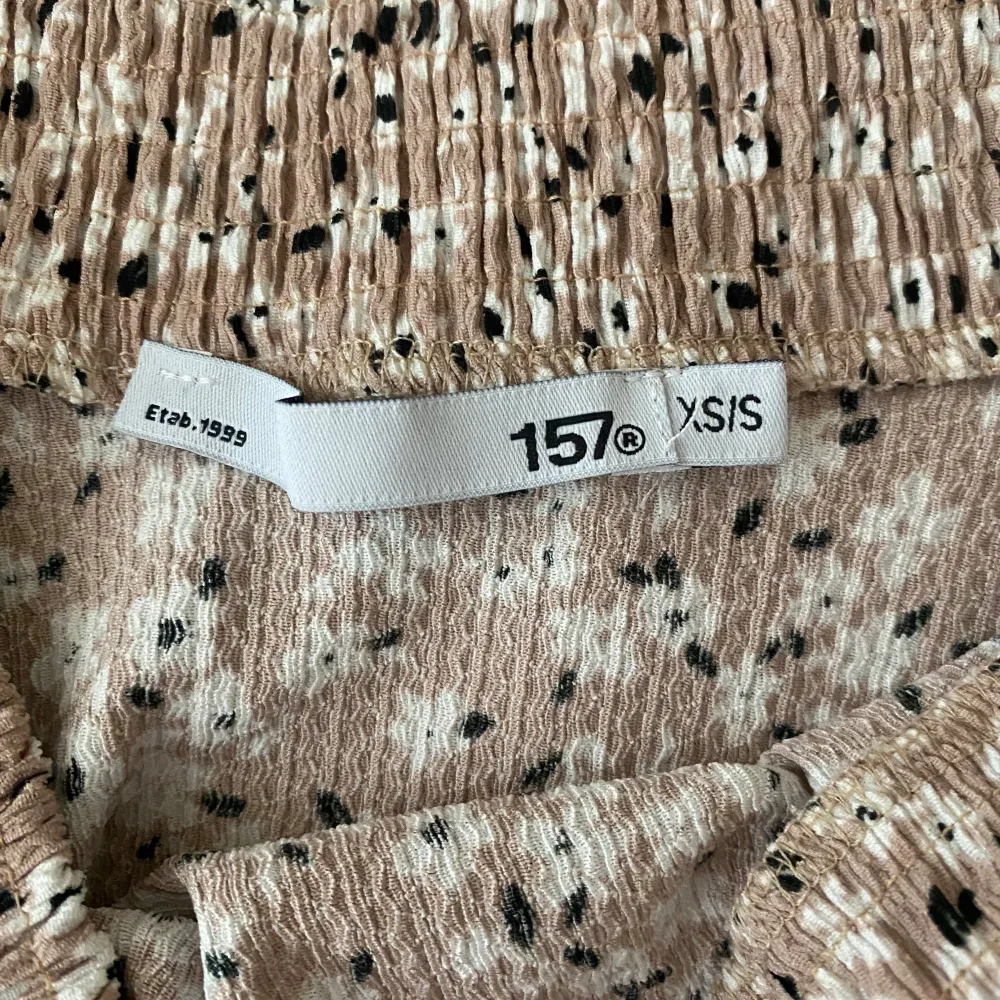 Söt beige kjol med blommigt mönster från 157. Kjolen har en elastisk midja för bekväm passform och är perfekt för en avslappnad stil. Den är kort och har ett lätt och luftigt material.. Hameet.