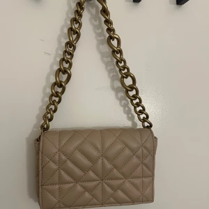 Zara axelväska med kedja - Snygg och classic beige axelväska från Zara med en guldig kedja som axelrem. Insidan är fodrad och har en praktisk ficka för småsaker.                  Den har används max 2 gånger, så är i väldigt bra och fint skick!