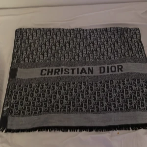Svart och grå halsduk från Christian Dior - Snygg och elegant halsduk från Christian Dior i svart och grått med ett klassiskt mönster och logotyp. Perfekt för att ge en lyxig touch till din outfit. Den har fransar i ändarna som ger en extra detalj.