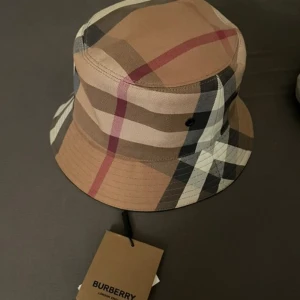 Burberry Bucket Hatt - Burberry bucket hatt perfekt nu inför våren och sommaren, köpt förra sommaren använd cirka 4 gånger, säljer då den ej kommit till användning.