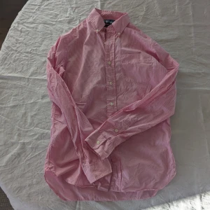 Rosa randig skjorta från Ralph Lauren - Säljer en stilren rosa randig skjorta från Ralph Lauren. Skjortan har långa ärmar och klassisk krage med knappar. Perfekt för en snygg och avslappnad look.