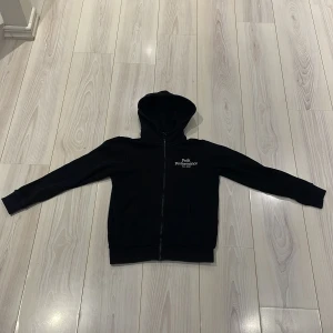 Svart hoodie från Peak Performance - Säljer en stilren svart hoodie från Peak Performance med dragkedja och broderad logga på bröstet. Perfekt för en avslappnad look. Huvan ger extra komfort och värme. Billigt pris!!!