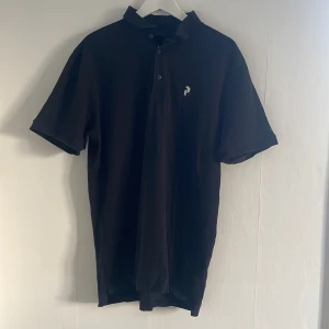 Svart pikétröja från Peak Performance - Säljer en stilren svart pikétröja från Peak Performance i storlek XL. Tröjan har korta ärmar och en klassisk krage med knappar. Perfekt för en avslappnad men ändå snygg look.