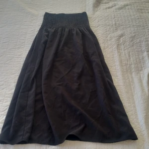 Svart långkjol från Gina Tricot - Snygg svart långkjol från Gina Tricot i storlek XS. Kjolen har en elastisk midja med smockdetaljer som ger en bekväm passform. Perfekt för en stilren look. Man kan även använda den som strapless klänning! Möts bara upp. Nypris 400kr