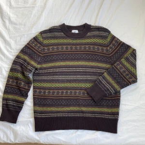 Snygg mönstrad stickad tröja - Säljer en snygg och skön mönstrad tröja från H&M i bruna och gröna toner. Tröjan har ett klassiskt mönster med inslag av gult och beige, perfekt för kyligare dagar. Den har långa ärmar och en rund halsringning.