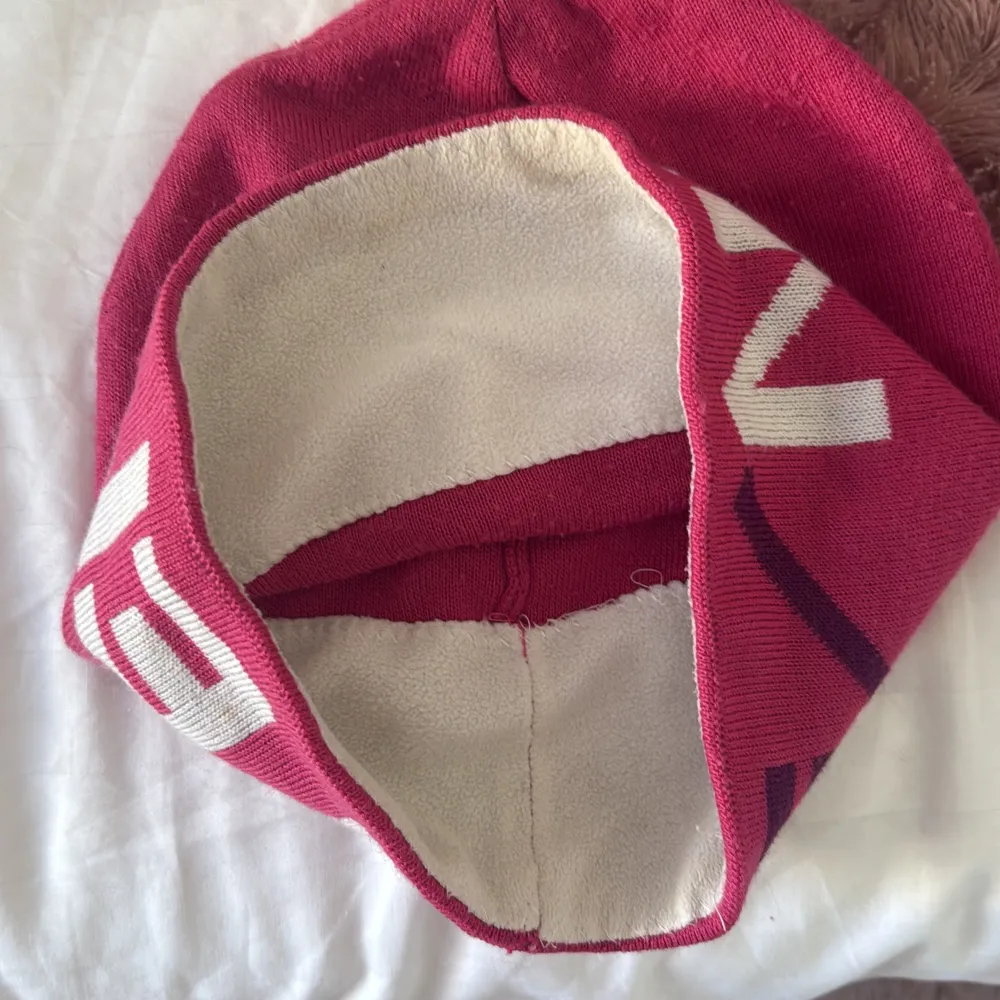 rosa mössa med vit text och mörkare detaljer. Perfekt för kyliga dagar med sitt mjuka och varma material. Den har en enkel och stilren design som passar till det mesta.. Asusteet.