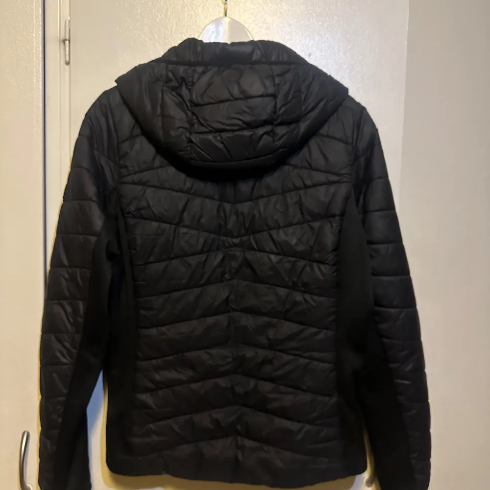 Säljer en snygg svart dunjacka från Barbour med huva och dragkedja. Jackan har en quiltad design och är perfekt för kyligare väder. Den har en stilren look med Barbour-logga på ärmen. Perfekt för dig som vill hålla stilen i vinter!. Takit.