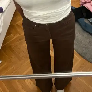 Snygga bruna jeans med hög midja och raka ben. De har en klassisk design med knappar och dragkedja framtill. Perfekta för en stilren look.