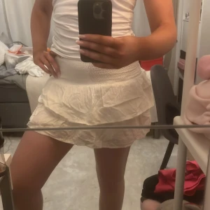 Vit kjol med volang - Söt vit kortkjol med volangdetaljer. Perfekt för varma dagar med sin luftiga design och elastiska midja för bekväm passform.