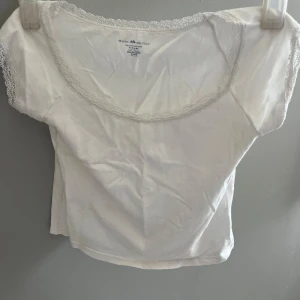 Vit topp med spetsdetaljer från Brandy Melville - Säljer en söt vit topp från Brandy Melville med spetsdetaljer längs halsringningen och ärmarna. Toppen har en rund hals och korta ärmar, jätte skön! Prislapp kan diskuteras💕