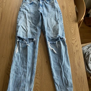 Blå jeans från Gina Tricot - Snygga ljusblå jeans från Gina Tricot med slitna detaljer på knäna. De har en klassisk femficksdesign och är tillverkade i hållbar bomull. Perfekta för en avslappnad stil.