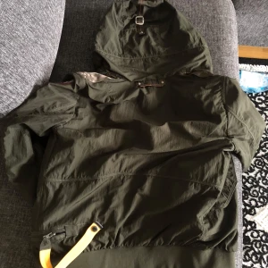 Grön jacka från Parajumpers - Snygg grön jacka från Parajumpers med huva och flera praktiska fickor. Jackan har en dragkedja framtill och en gul detalj vid kragen. Perfekt för en cool och avslappnad stil. Ny pris ca 5500kr