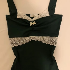 Coquette Kalilah top (REDUCERAT PRIS) - Ursprungligt pris: 649-, En coquette och supersöt handgjord topp 🤍 Kalilah Top i stretchigt bomullstyg  Guldhjärtat är rostfritt stål   • Mjuk, mörkgrön bomull med stretch • Passar XS till S • Begränsad upplaga – säljer snabbt slut! • Bedårande vit spets • Söt vit rosett med ett gyllene hjärta • Vintageinspirerad   #handsydd #handmade #coquette #aesthetic #trendy #tiktok #top #lacetop #lace #sløyfetopp #sløyfe #läcker #angeliclove