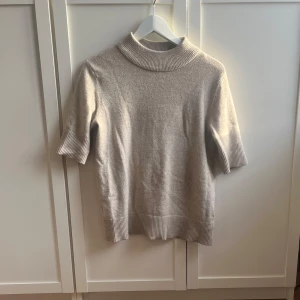 Beige kortärmad - Säljer en stilren beige polotröja med korta ärmar. Tröjan har ribbade detaljer vid krage, ärmslut och nederkant. Perfekt för en avslappnad och elegant look. Passar Xs och S