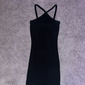 Svart klänning med korsade axelband - Snygg svart klänning med korsade axelband. Perfekt för en stilren look. Klänningen har en tight passform och är tillverkad i ett mjukt material som ger en bekväm känsla.