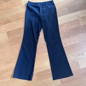 Svarta byxor från Mexx - Snygga svarta byxor från Mexx med diskret mönster. Byxorna har en rak passform och är perfekta för en stilren look. De är högmidjade och har en klassisk design med hällor för bälte.