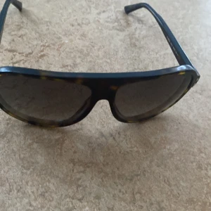 Solglasögon från Emporio Armani - Snygga solglasögon från Emporio Armani med en cool leopardmönstrad båge. De har en klassisk design med breda skalmar och mörka linser. Perfekta för att ge en stilren touch till din look.