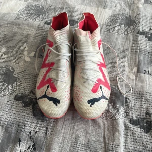  Puma future ultimate FG Elite  - Snygga fotbollsskor från Puma i vitt med rosa detaljer och svarta logotyper. Skorna har snörning och en modern design som passar perfekt för fotbollsplanen.