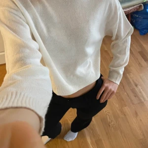 Vit stickad tröja - Säljer en stilren vit stickad tröja med croppad passform. Tröjan har långa ärmar och ribbade kanter vid ärmslut och nederkant. Perfekt för en avslappnad look.
