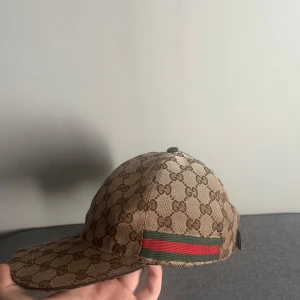 Gucci keps  - Snygg beige keps från Gucci med klassiskt monogrammönster och röd-gröna detaljer på sidan. Perfekt för att ge din outfit en lyxig touch. Justerbar passform för optimal komfort. Priset kan diskuteras fraktar inom 24 h 