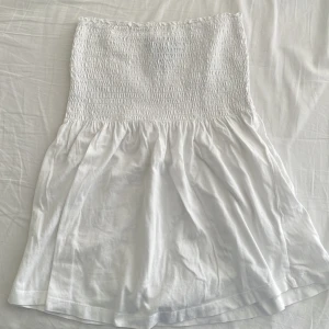 Vit axelbandslös topp - Söt vit axelbandslös topp med smockdetaljer upptill. Perfekt för varma sommardagar. Den har en luftig och bekväm passform som ger en avslappnad look.