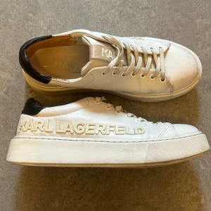 Vita sneakers från Karl Lagerfeld - Snygga vita sneakers från Karl Lagerfeld med svart detalj vid hälen och märkets namn i relief på sidan. Skorna har klassisk snörning och en stilren design som passar perfekt till vardagsoutfiten. Dom är lagade i hälen på insidan hos skomakare.