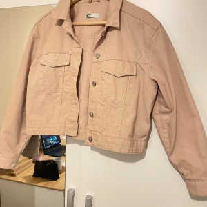 Beige jeansjacka från Gina trico - Snygg beige jeansjacka från Ginamed knappar framtill och klassisk krage. Jackan har två bröstfickor med lock och en croppad passform. Perfekt för en avslappnad stil.