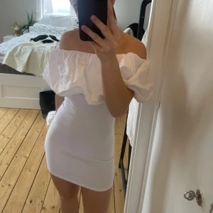 Vit offshoulder klänning - Säljer en stilren vit offshoulder klänning med kort längd och massa puff upp till axlarna. Klänningen har en tight passform och är perfekt för somriga tillfällen. Den är tillverkad i ett ribbat material som ger en snygg struktur. Perfekt till avslutning eller student