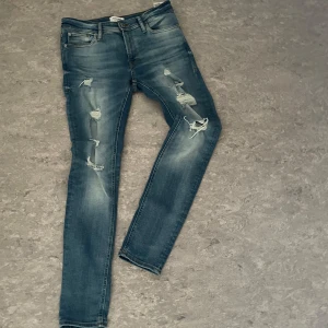 Jack & Jones blåa jeans - Säljer ett par snygga Jack & Jones Jeans med slitningar som ger en trendig look. Jeansen är storlek 30/32. Om det finns frågor är det bara att ställa!
