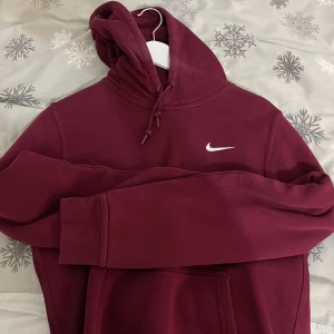 Vinröd hoodie från Nike - Säljer en snygg vinröd hoodie från Nike med klassisk logga på bröstet. Tröjan har långa ärmar och en praktisk magficka. Perfekt för kyliga dagar! Pris kan diskuteras!!