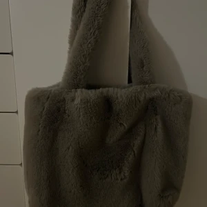 Grå pälsväska - Mysig och fluffig grå väska som rymmer exempelvis en dator och annat som önskas. Present och därför osäker vart den är köpt. Ingen äkta päls. Bra med flickor och utrymme inuti 