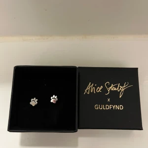 Söta örhängen från Alice Stenlöf x Guldfynd - Charmiga örhängen i form av tassavtryck från Alice Stenlöf x Guldfynd. De är i silverfärg och kommer i en elegant svart ask. Perfekta för djurälskare som vill ha en subtil men stilren accessoar. Oanvänd, silver 925 