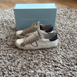 Philippe model skor - Snygga vita sneakers från Philippe Model med lite blåa detaljer.  Skorna är i bra sick och ingår med dust bag och box allt og. Hör av er vid funderingar!