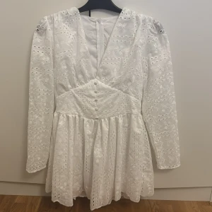 Vit spetsklänning - Charmig vit klänning med spetsdetaljer och v-ringad design. Klänningen har långa ärmar och en dragkedja i ryggen. Perfekt för STUDENT👏🍾