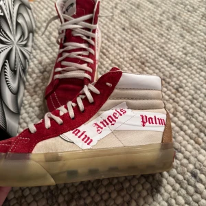 Vans Sk8-Hi Reissue Palm Angels Chili Pepper - Snygga Vans Sk8-Hi Reissue i samarbete med Palm Angels. Skorna har en cool röd och beige design med Palm Angels-logga på sidan. De är höga med snörning och har en genomskinlig sula. Perfekta för att ge din outfit en unik touch. Priset kan diskuteras👍
