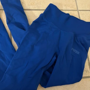 Blå leggings från Fuze - Snygga blå leggings från Fuze i en tight passform. Perfekta för träning med hög midja och ribbade detaljer. Materialet är stretchigt och bekvämt, vilket gör dem idealiska för aktiva dagar. Aldrig använda för att jag har för mycket tränings tights.