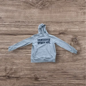 Grå hoodie från 157 - Säljer en grå hoodie från 157 med texten 'Vancouver Sports Dept.' på framsidan. Tröjan har en klassisk design med huva och långa ärmar. Perfekt för en avslappnad stil.