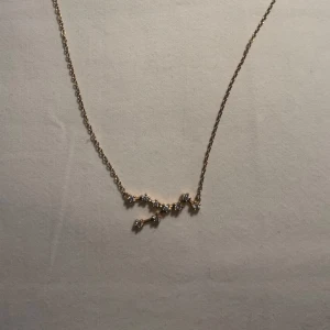 Guldhalsband med stjärntecken oxen - Guldhalsband från SAFIRA med oxen(taurus) stjärntecken i fint guld och små ädelstenar! Elegant guldhalsband med ett hänge, jedjan är tunn och smidig, perfekt för att bära varje dag. Lyxigt och elegant halsband!