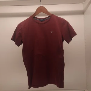 Röd t-shirt från GANT - Snygg vinröd t-shirt från GANT med korta ärmar och rund halsringning. Den har en liten broderad logotyp på bröstet. Perfekt för en avslappnad stil.