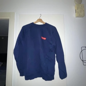 Mörkblå sweatshirt från vintage  - Säljer en mörkblå sweatshirt från vintage med rund hals och långa ärmar. Tröjan har en enkel design med VELUX-loggan i rött på bröstet. Perfekt för en avslappnad stil.