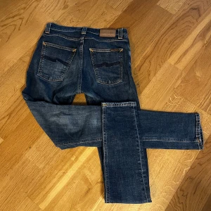 Blå jeans från Nudie Jeans - Säljer ett par snygga blå jeans från Nudie Jeans. De har en klassisk femficksdesign med orange sömmar och en knappgylf. Perfekta för en avslappnad stil. Priset är inte hugget i sten!