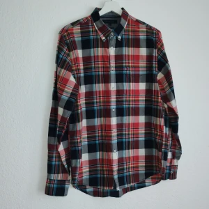 Rutig skjorta från Tommy Hilfiger - Snygg rutig skjorta från Tommy Hilfiger i New York Fit. Skjortan har ett klassiskt rutmönster i rött, blått och vitt med långa ärmar och knappar framtill. Perfekt för en stilren look.