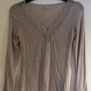 Beige långärmad tröja från Intimissimi - Säljer en beige långärmad tröja från Intimissimi med v-ringning och spetsdetaljer. Tröjan är tillverkad i ett mjukt material med kashmir, perfekt för en stilren look. 