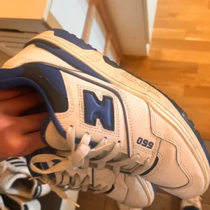 New Balance 550 sneakers - Säljer ett par New Balance 550 sneakers i vitt och blått. Skorna har en klassisk design med snörning och är i skinnmaterial. Perfekta för både vardag och träning. De är i bra skick och redo för en ny ägare!
